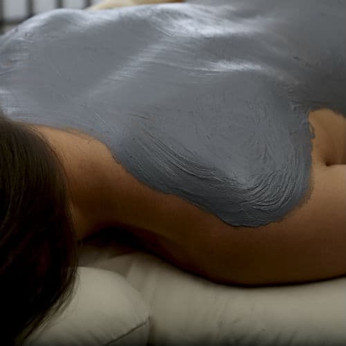 A grey clay body mask applied to a client's back and shoulders