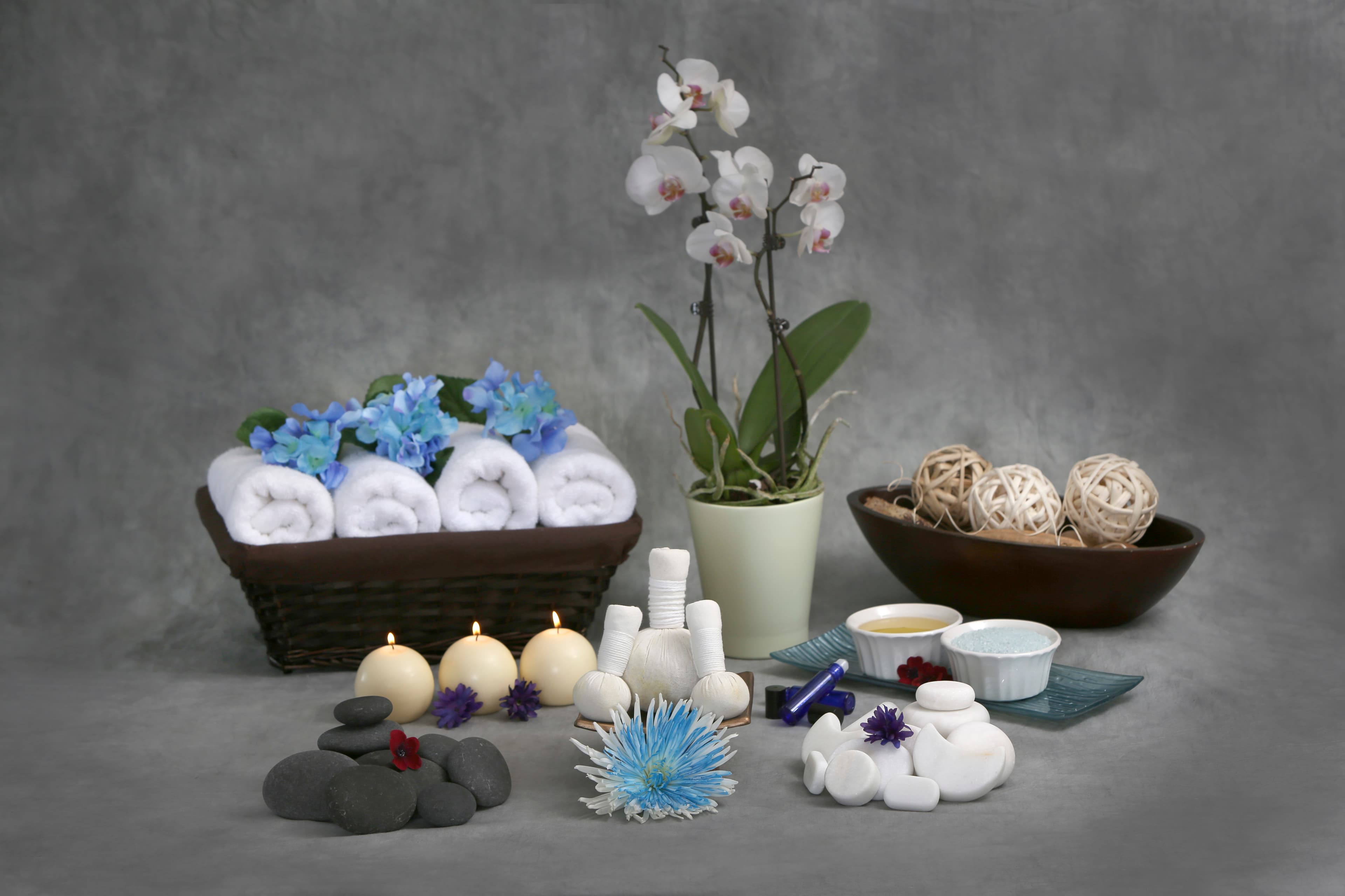 A spa still life with rolled white towels, an orchid, lit candles, and hot stones