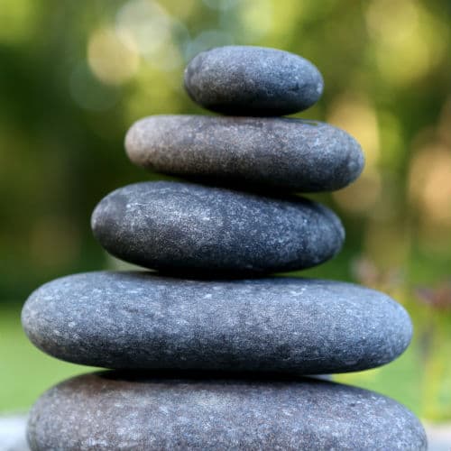 A stack of smooth massage stones with a blurred green outdoor background