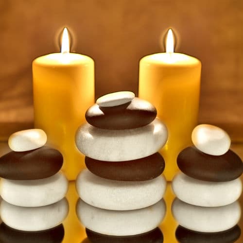 Warm pillar candles beside a stack of hot and cold massage stones
