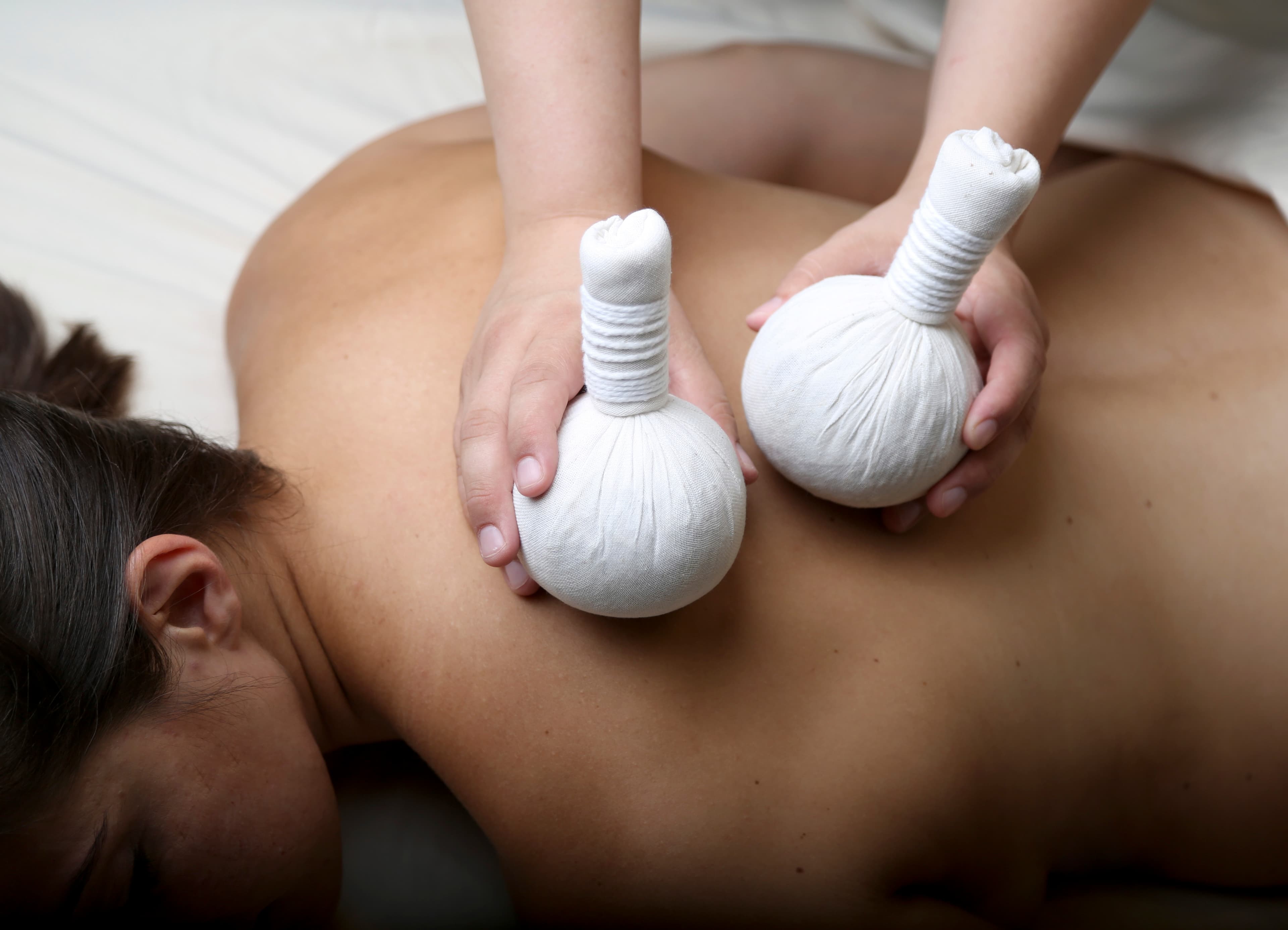 A therapist pressing herbal compress balls into a client's back