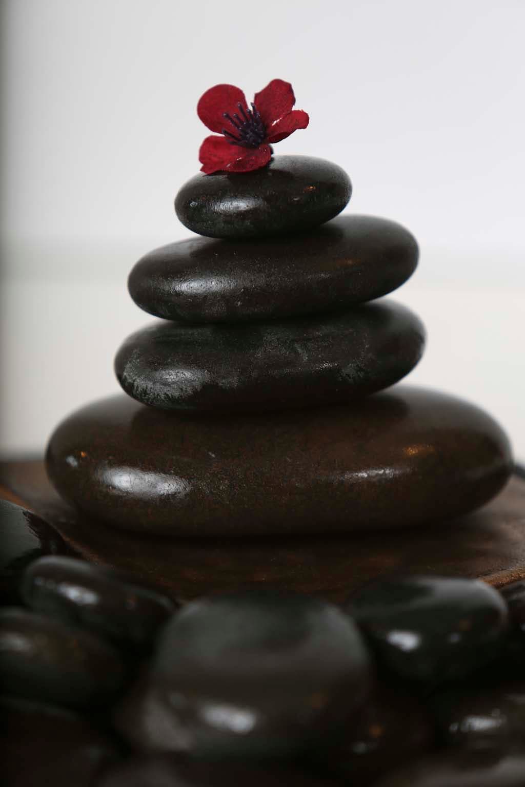 A small stack of black massage stones topped with a red flower