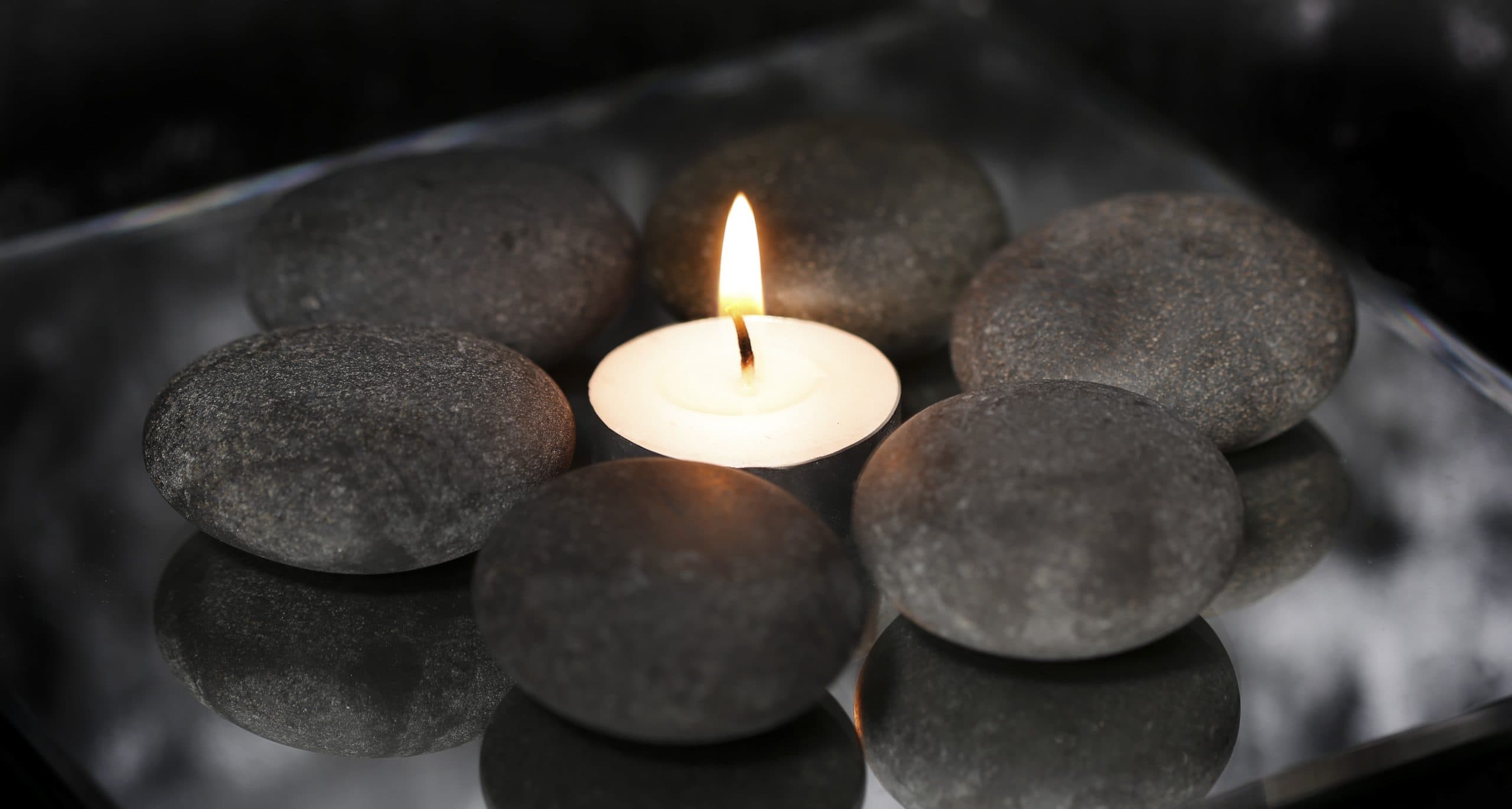 Grey massage stones arranged around a lit tealight candle